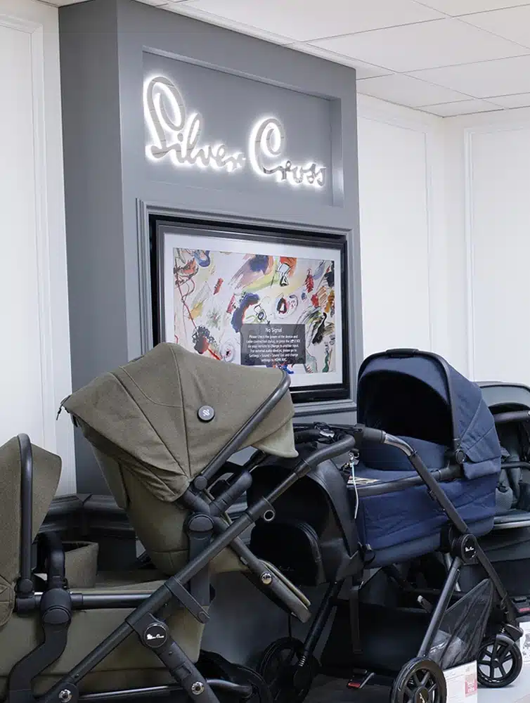 Display area for baby strollers with illuminated "Silver Cross" sign and "DUNE" & "REEf" pushchair posters.