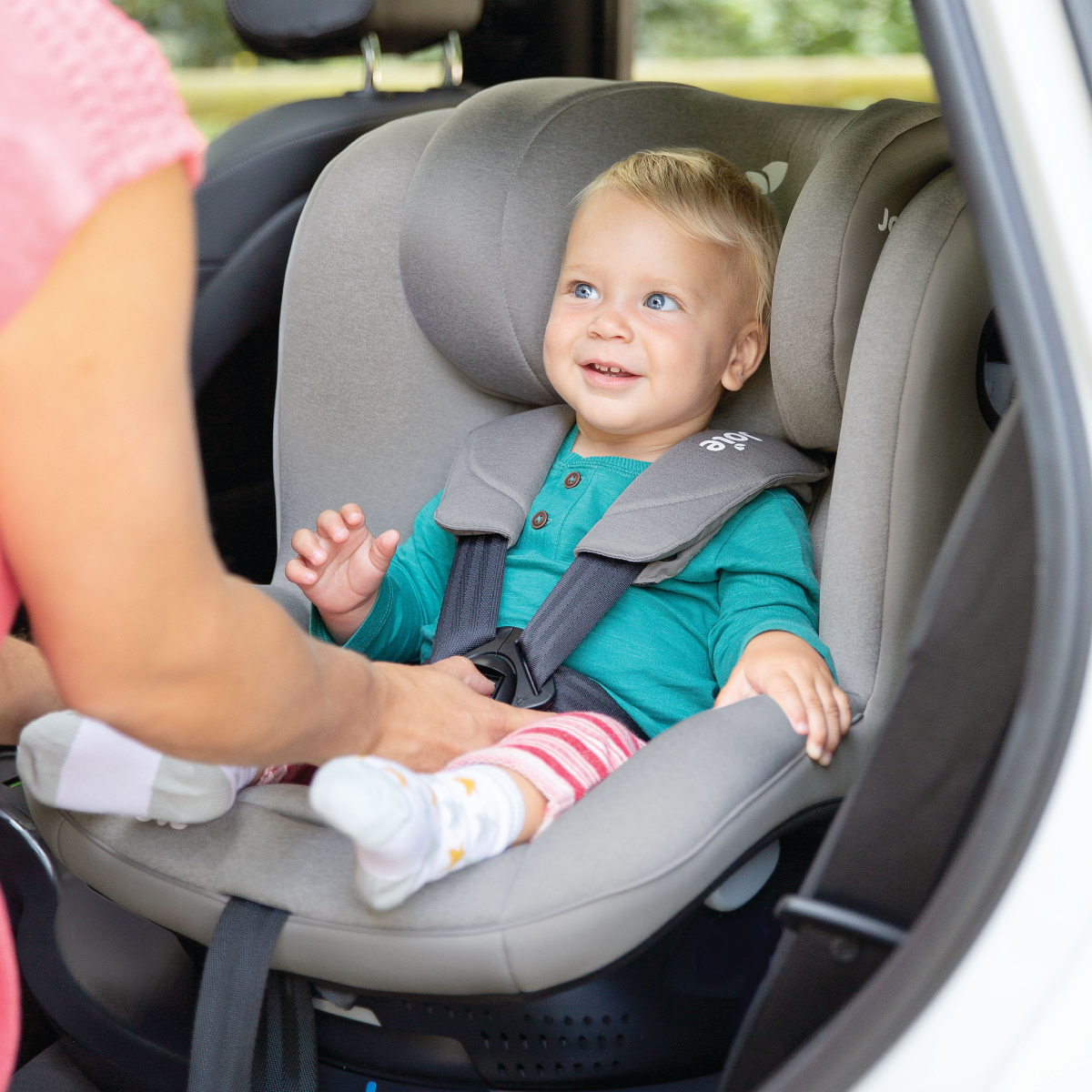 Parent strapping a toddler onto their car seat.